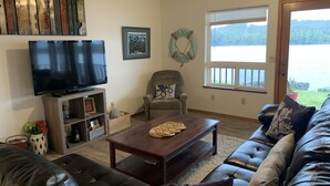 A living room with a large flat-screen TV, a grey armchair, a dark brown coffee table, and a black leather sofa. - Waterfront only 2 miles from downtown!  Sleeps 8. Amazing Views! (Ketchikan)