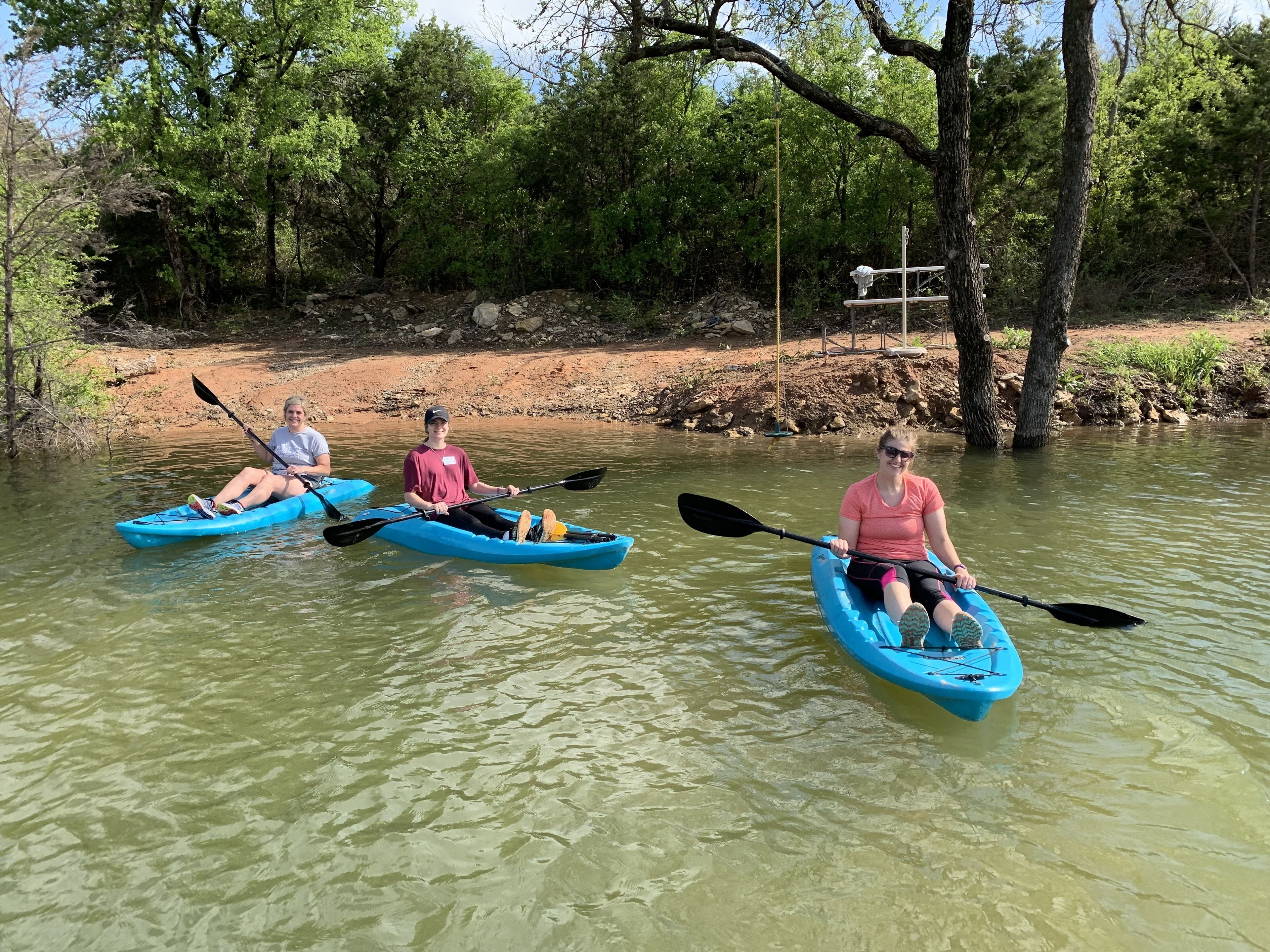 Three people kayaking on a calm river surrounded by trees.