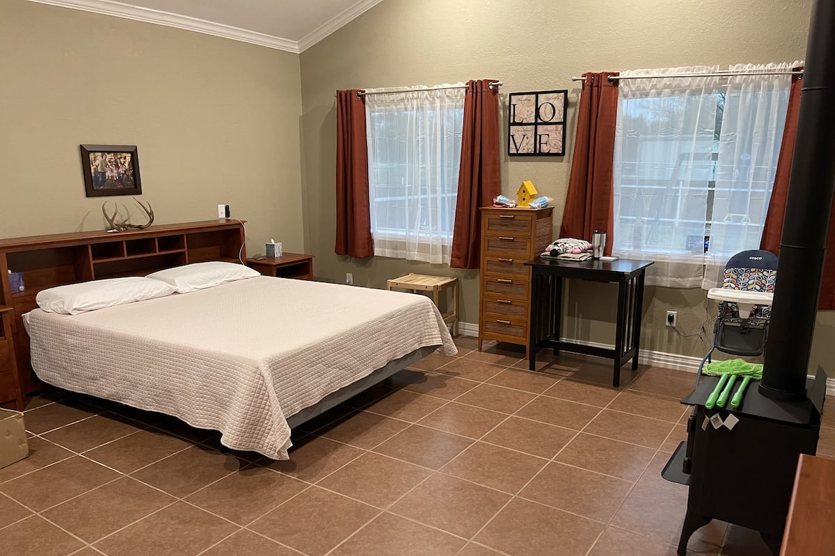 A bedroom with a bed, a dresser, a nightstand, a wooden cabinet, a small table, a chair, a stroller, and a heater.