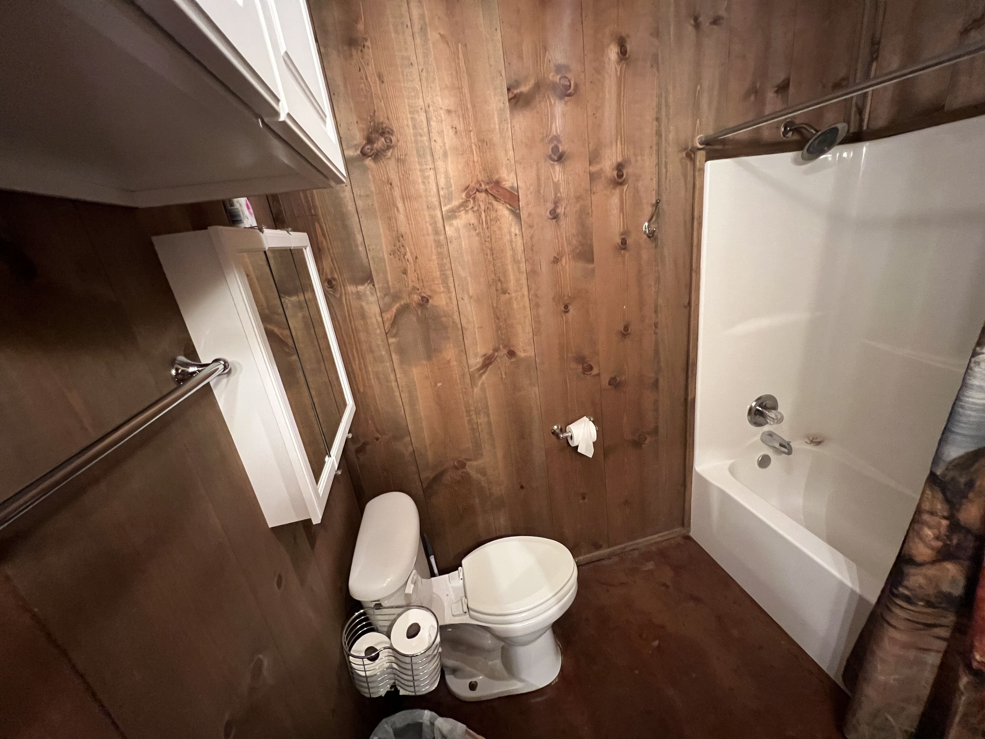 A bathroom with wooden walls, a toilet, a shower, and a handrail.