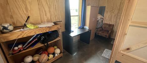 Una habitación de madera con un escritorio, estantes llenos de balones deportivos, una silla y un armario.