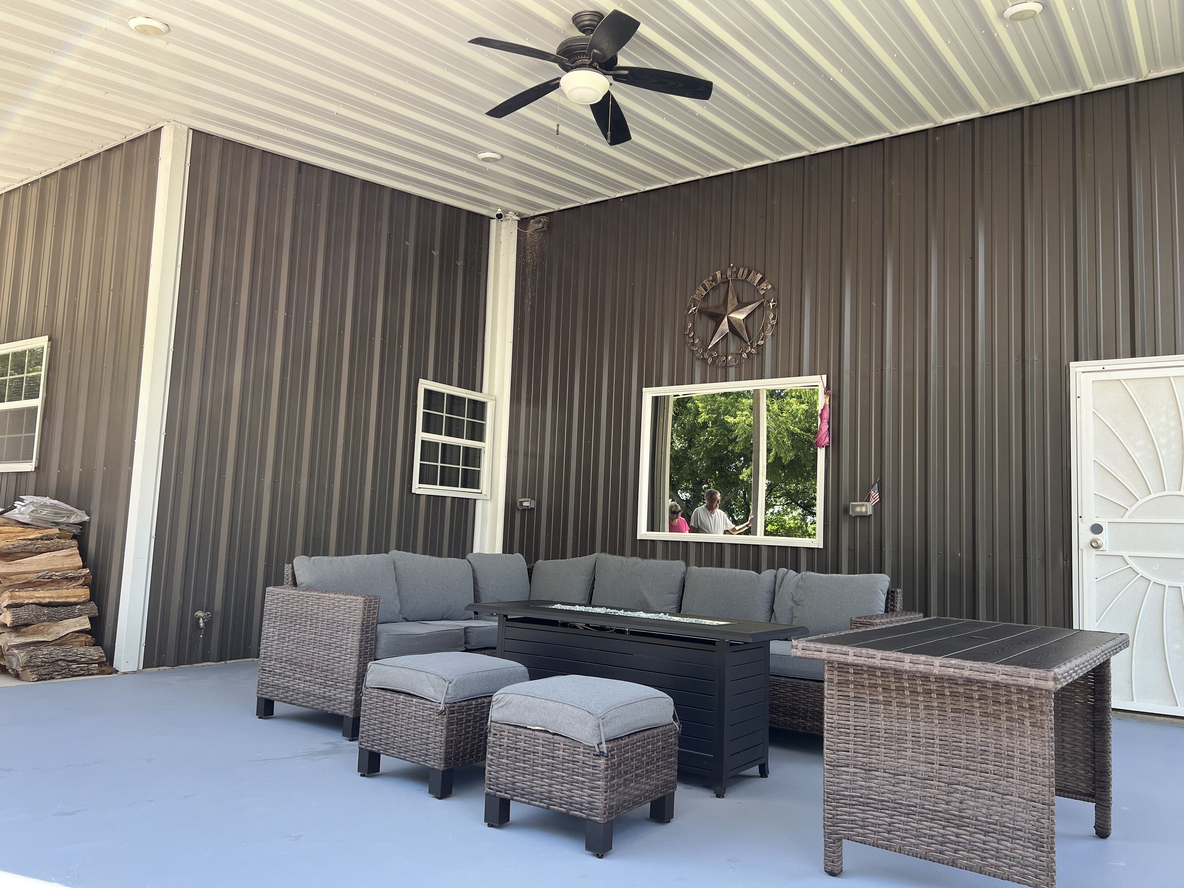A covered outdoor seating area with a sectional sofa, ottomans, and a table.