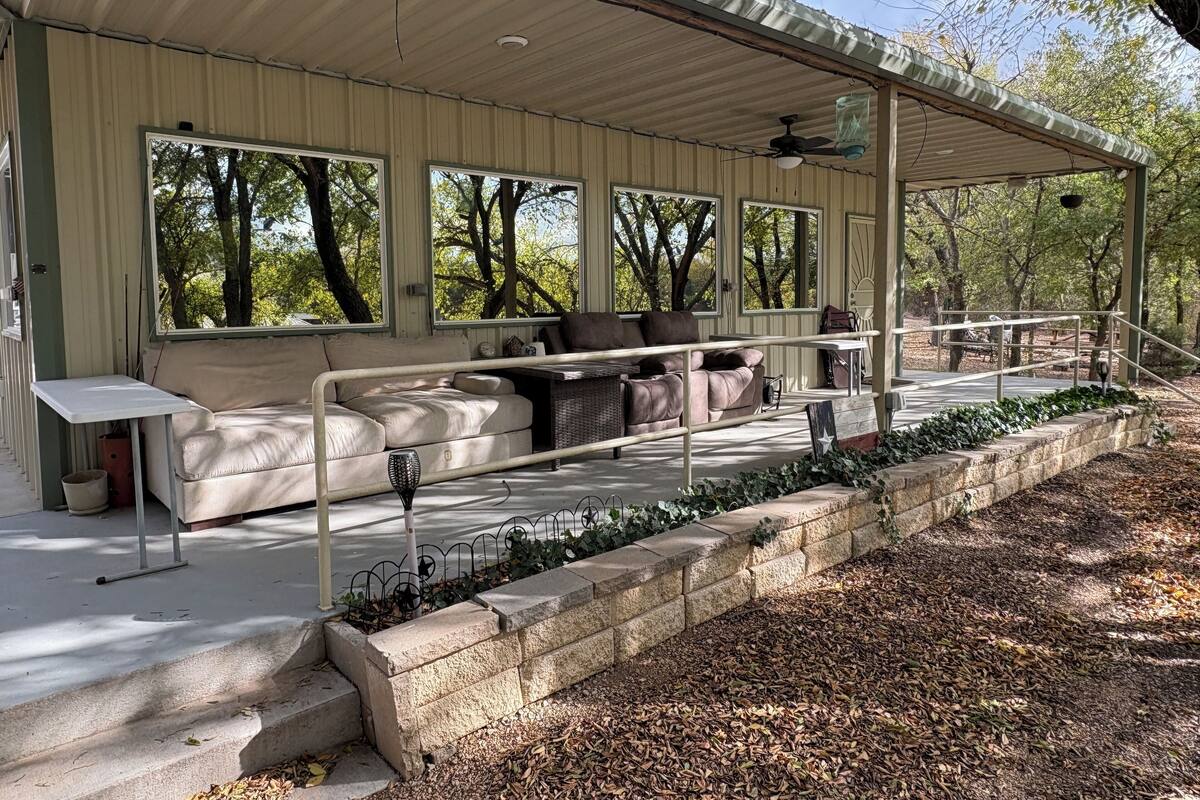 A covered outdoor seating area with a sofa and table, surrounded by stone walls and a wooden deck.
