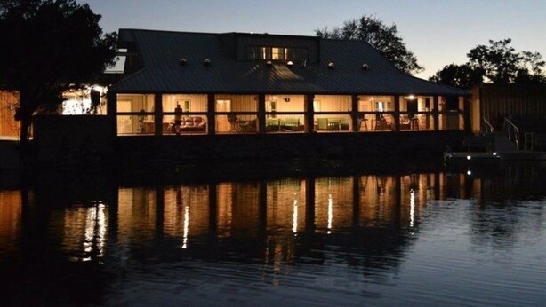 Un bâtiment situé au bord de l’eau, doté de nombreuses fenêtres qui se reflètent dans l’eau.