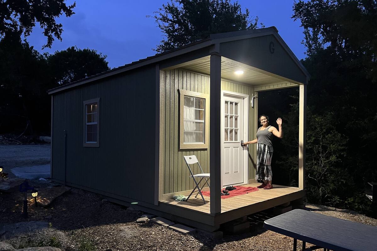 A small, single-story shed with a door and windows, a bench outside, and a small table.