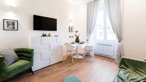 A modern living room with a flat-screen TV, a green sofa, a dining table with chairs, and a large window with curtains. - Charming Trastevere home overlooking a medieval church: suite, 3 baths, WiFi, AC (Roma)