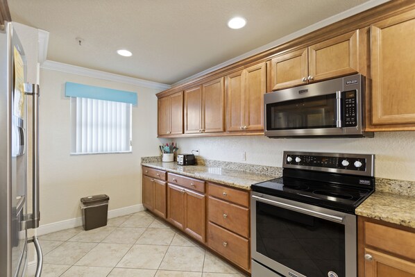 A kitchen with wooden cabinets, a stainless steel microwave, and an oven.