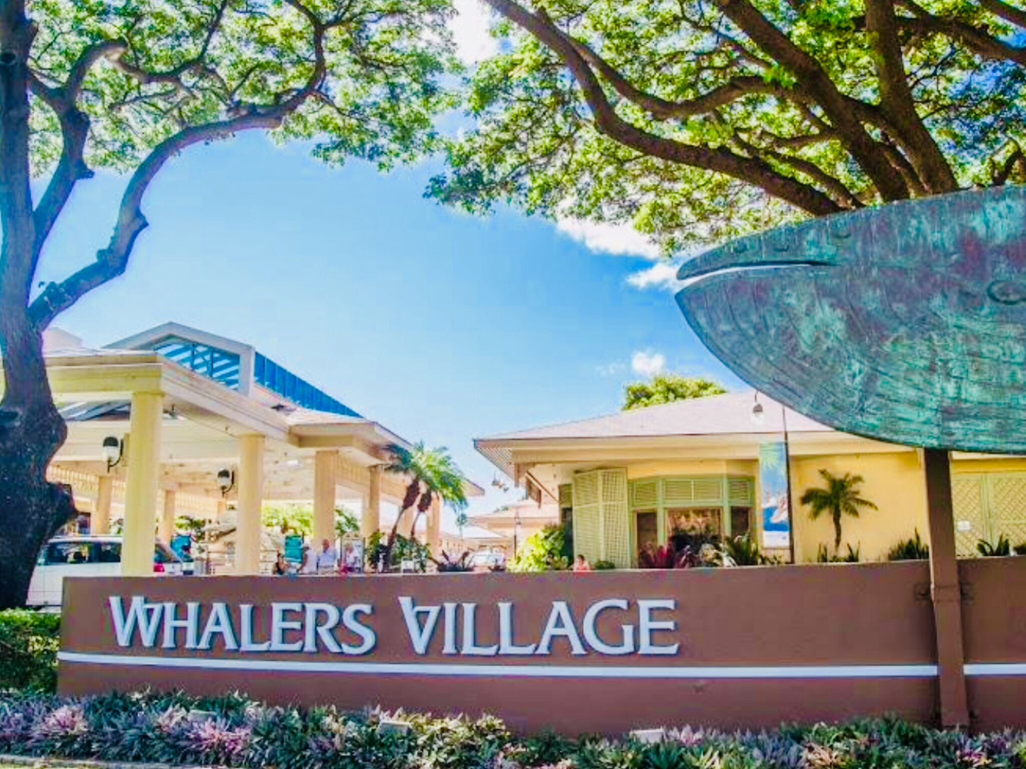 A sign for Whalers Village with a clear view of the surrounding buildings and a large decorative metal structure.