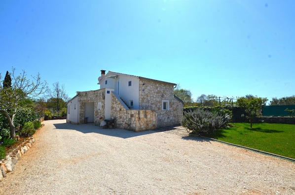 A stone building with a gravel driveway and a green lawn.