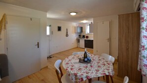 A small, open-plan living and dining area with a round table set for two, a kitchen in the background, and a wooden door on the right. - Bavica Apartment with private parking (Rovinj)