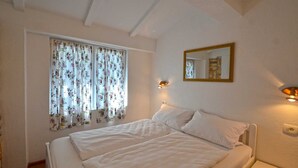 A bedroom with a bed, a window with floral curtains, a wall-mounted mirror, and bedside lamps. - Bavica Apartment with private parking (Rovinj)