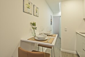 Un comedor con una mesa blanca preparada para dos, un florero con planta y cuadros en la pared.