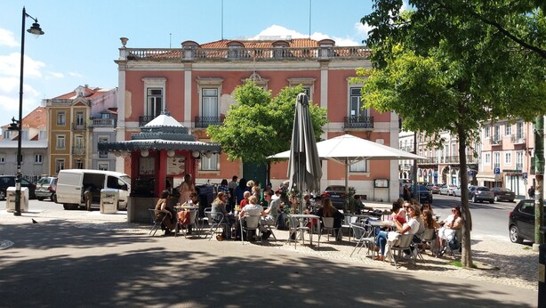 A street scene with outdoor seating at a cafe, surrounded by historic buildings with balconies and a red-tiled roof. - OLD TOWN PRÍNCIPE REAL - Apart. modern with patio and direct access to quiet street. (Lisboa)