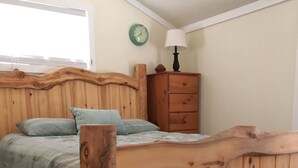 Una cama de madera con cabecera, una mesita de noche con lámpara y un reloj en la pared.