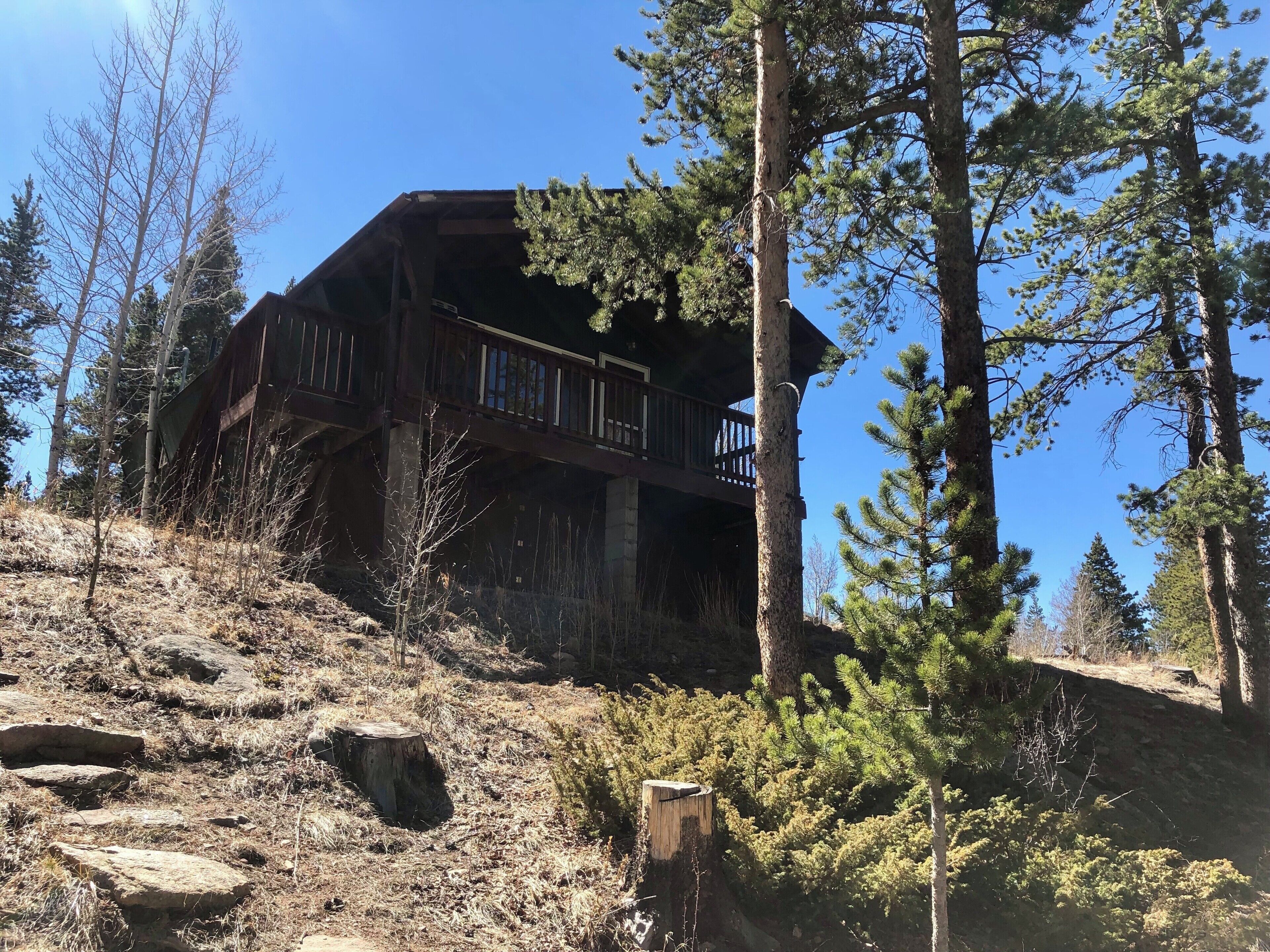 A cabin with a balcony, surrounded by trees and a rocky hillside.