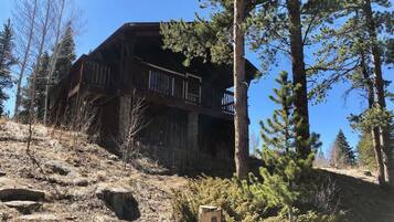 A cabin with a balcony, surrounded by trees and a rocky hillside.