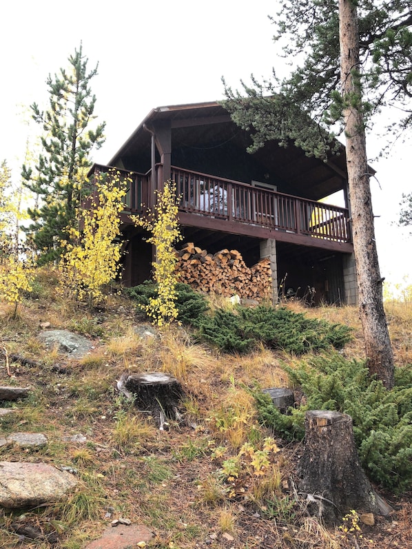 A cabin with a balcony, surrounded by trees and a pile of firewood.