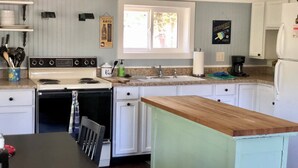 Una cocina con gabinetes blancos, encimera de madera, estufa, fregadero y ventana.