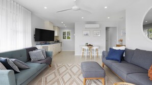 Ein modernes Wohnzimmer mit grauem Sofa, blauem Sofa und einem Essbereich mit weißem Tisch und Stühlen.