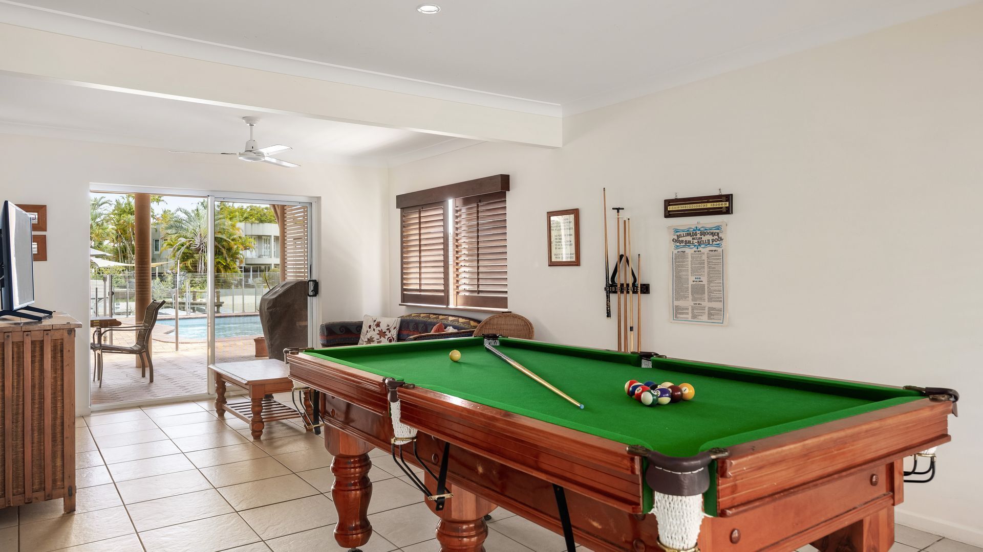 Une table de billard avec des billes, une queue de billard et un recueil de règles encadré accroché au mur.