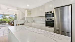 A modern kitchen with a large marble countertop, stainless steel appliances, and a view of the outdoors.