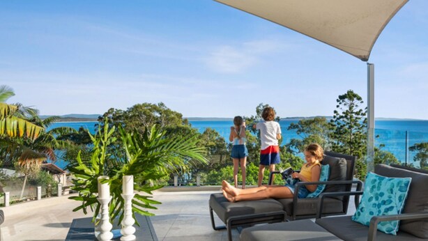 A patio with outdoor seating, a view of the sea, and tropical vegetation.
