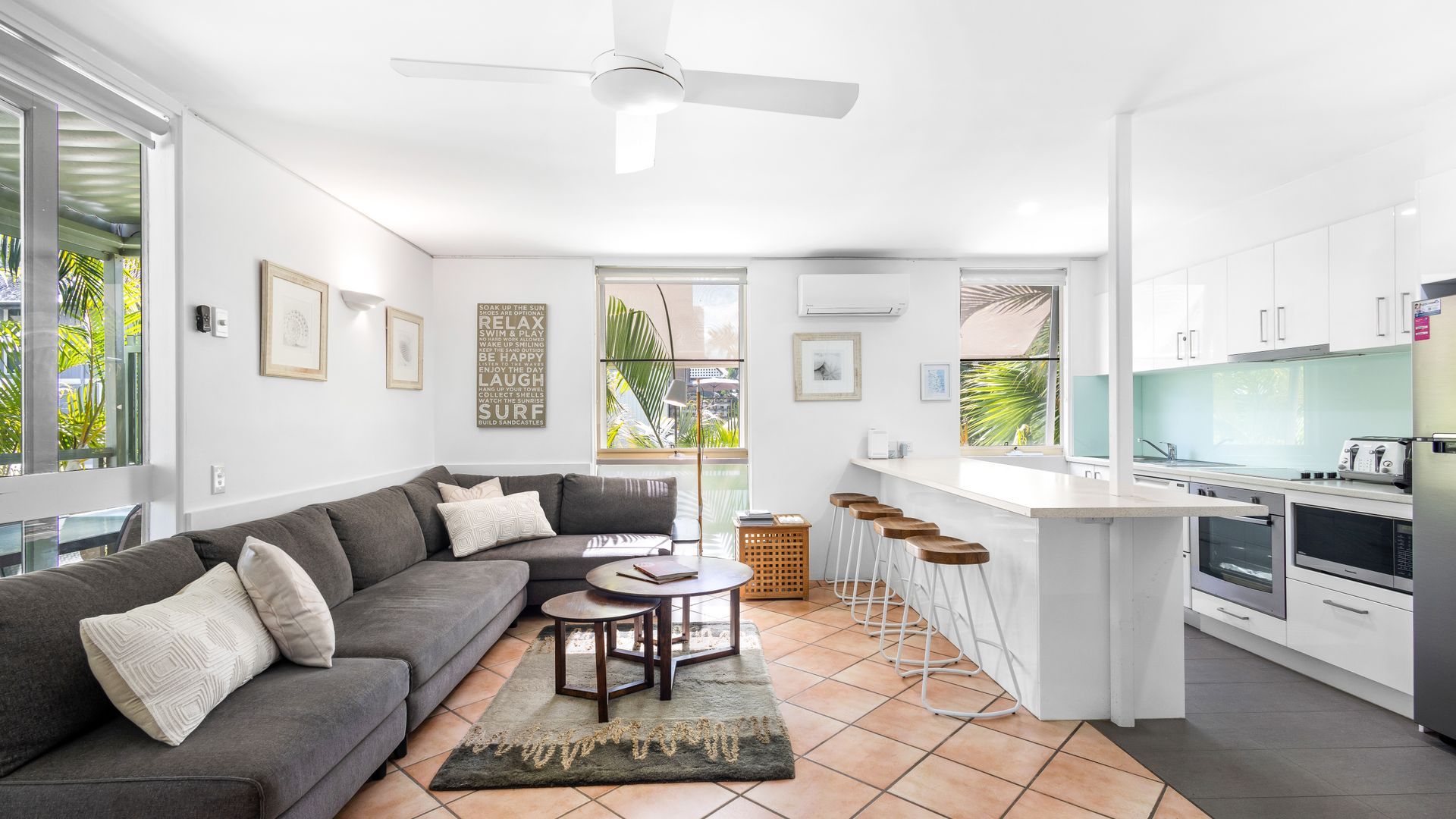 A modern kitchen with white cabinets, a bar area, and a dining space with a gray sofa and a coffee table.
