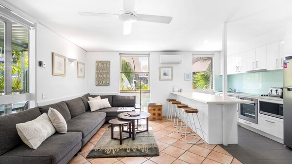 A modern kitchen with white cabinets, a bar area, and a dining space with a gray sofa and a coffee table.