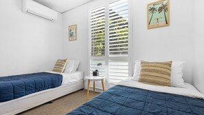 Ein Zimmer mit zwei Betten, einem kleinen Tisch und einem Fenster mit Jalousien.