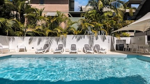 Una piscina con agua azul cristalina, rodeada de sillas reclinables blancas y palmeras.