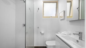Un baño moderno con cabina de ducha de vidrio, inodoro, lavamanos con espejo y ventana.