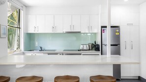 Eine moderne Küche mit weißen Schränken, einem Edelstahlkühlschrank und einem großen Fenster.