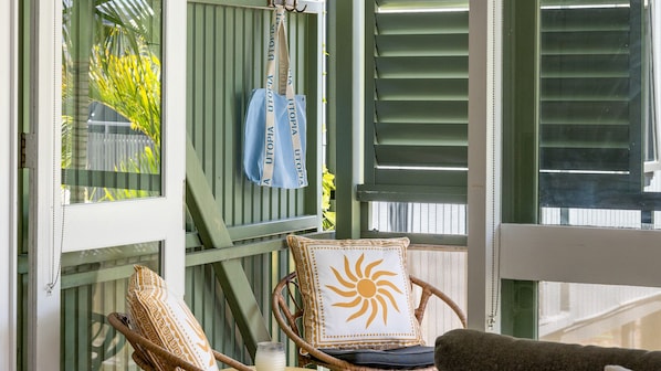 Habitación con vistas a una cerca verde, una silla de mimbre con un cojín solar, y un bolso colgante con una correa azul.