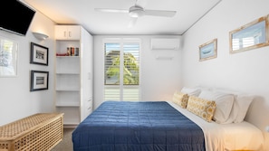 Un dormitorio con cama, armario, ventilador de techo, ventana con persianas y aire acondicionado de pared.