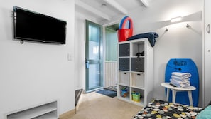 Ein Schlafzimmer mit einem Bett, einem an der Wand montierten Fernseher, einem Kleiderschrank, einem kleinen Tisch mit Handtüchern und einer Tür zu einem anderen Raum.