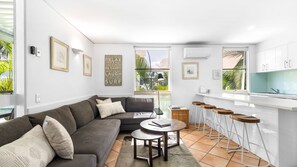 Ein modernes Wohnzimmer mit grauem Sofa, einem Couchtisch und einer Küchenzeile mit Barhocker.