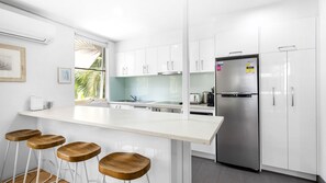 A modern kitchen with white cabinets, a stainless steel refrigerator, and a bar area with stools.