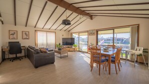 A spacious living area with a sofa, dining table, and chairs, a television, and large windows with a view.