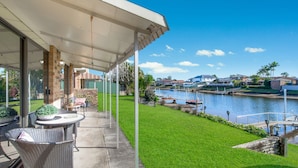 A covered patio with outdoor furniture, a view of a water body, and residential buildings in the background. - 29A Ballina Crescent, Port Macquarie (Port Macquarie)