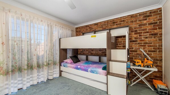 A bunk bed room with a brick wall, a window with sheer curtains, and a toy truck on a shelf. - 29A Ballina Crescent, Port Macquarie (Port Macquarie)