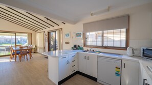 A modern kitchen with a large island, a dining area with a table and chairs, and a view of the outdoors through a sliding glass door.