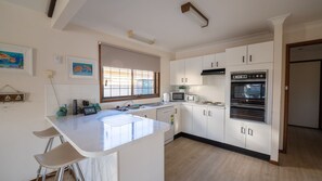 A modern kitchen with white cabinets, a stainless steel sink, and a built-in oven. - 29A Ballina Crescent, Port Macquarie (Port Macquarie)