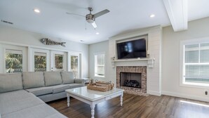 Una sala de estar con sofá, mesa de centro, chimenea, televisor y ventilador de techo.