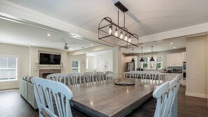 Un comedor amplio con una gran mesa rectangular, sillas blancas y un moderno candelabro.