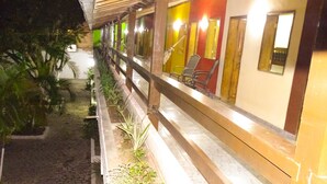 A corridor with a wooden railing, potted plants, and a series of doors with chairs inside. - Pousada Dom Hotel (Porto Seguro)