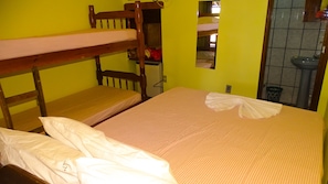Une chambre de dortoir avec des lits superposés, un lit simple, un miroir et une salle de bain équipée d’un lavabo et de toilettes.