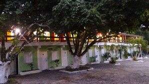 A building with multiple doors and windows, surrounded by trees and a paved area. - Pousada Dom Hotel (Porto Seguro)