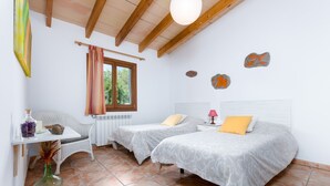 A bedroom with two beds, a window, a radiator, a table with a vase, and a hanging light fixture. - Villa with private pool near Manacor,  Villa con piscina privada en Manacor, YourHouse Garballons (Manacor)