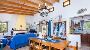A cozy room with a wooden dining table, chairs, a chandelier, a fireplace, and a kitchen area. - Villa with private pool near Manacor,  Villa con piscina privada en Manacor, YourHouse Garballons (Manacor)