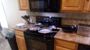 A kitchen with wooden cabinets, a black microwave, a stove, and various cooking utensils. - $89/night for 2 people, plus $20/night for each additional person (Pahrump)